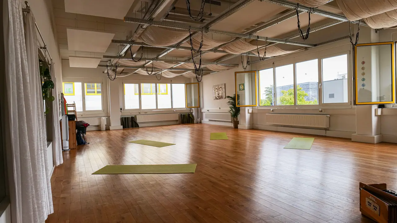 Der leere Studioraum mit Holzboden, Yogamatten und viel Tageslicht.